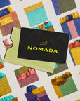 Nomada card on a fabric background with colorful patterns